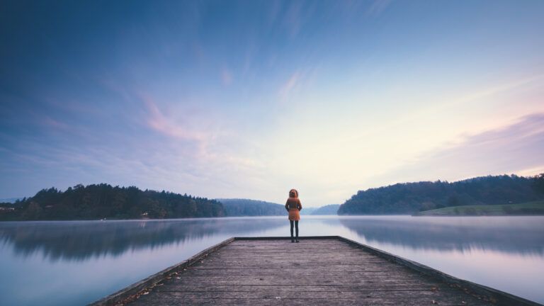 Peaceful lake scene with person looking out from jetty; Getty Images
