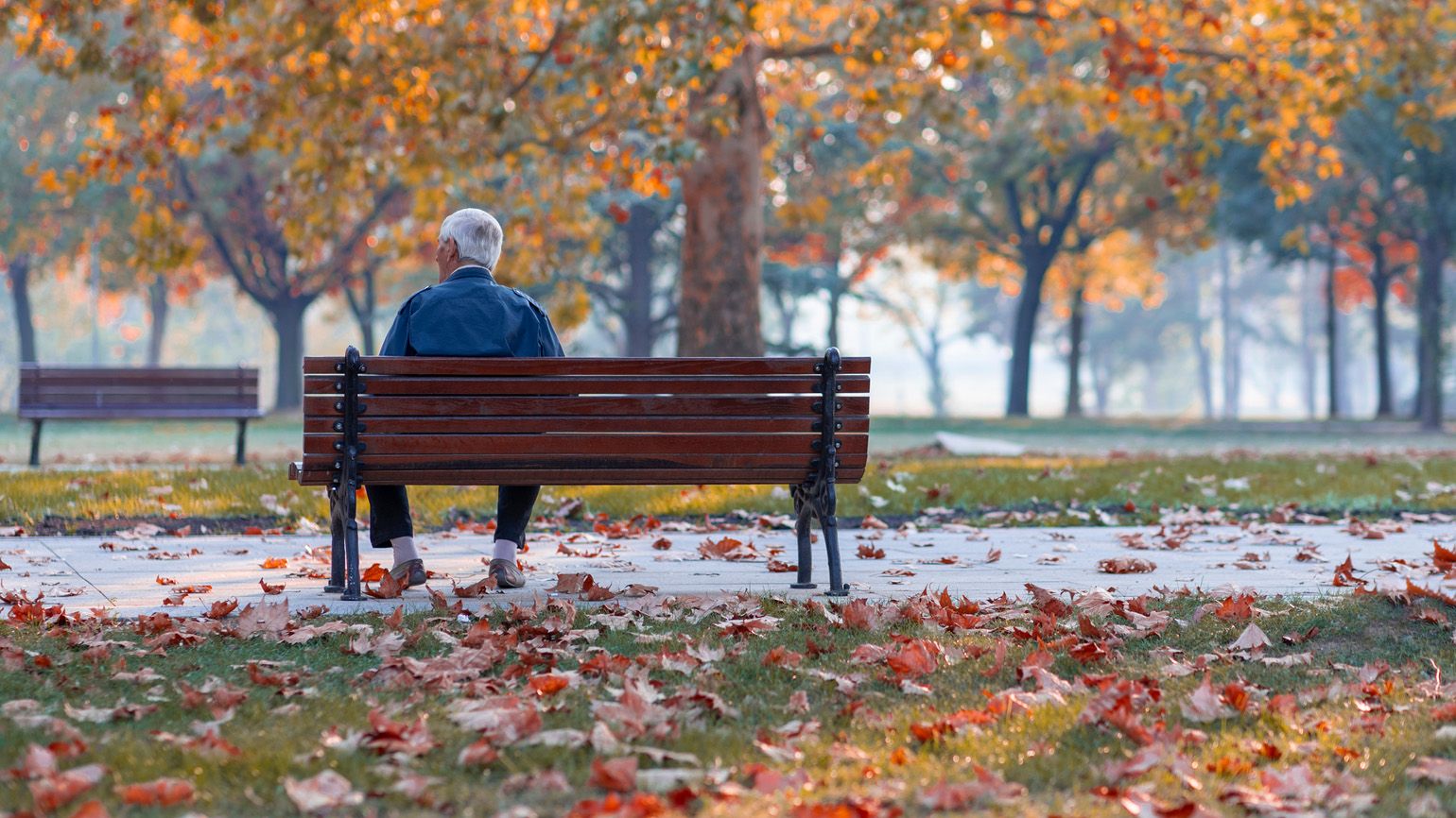 Senior citizen man sitting alone on a bench during Autumn season; Getty Images