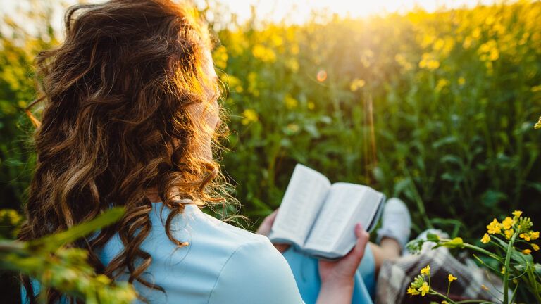 A woman reads her Bible in a field of yellow flowers
