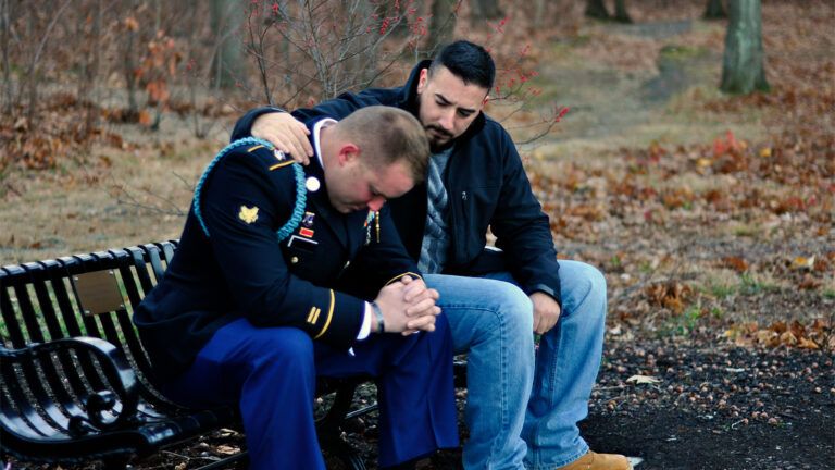 A man prays with a member of the military