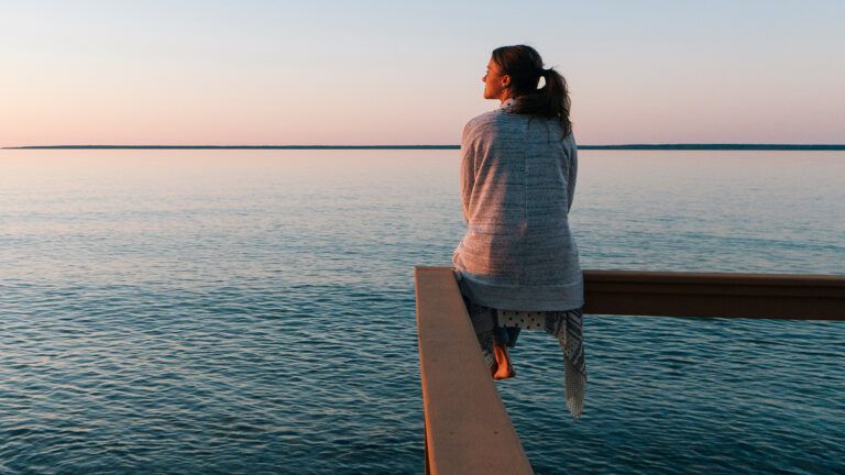 A woman sits on a lakeside pier at sunrise