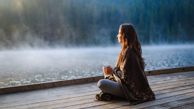 Woman relaxing with a cup of coffee in the nature stock photo. Woman drinking coffee near a lake in the morning.