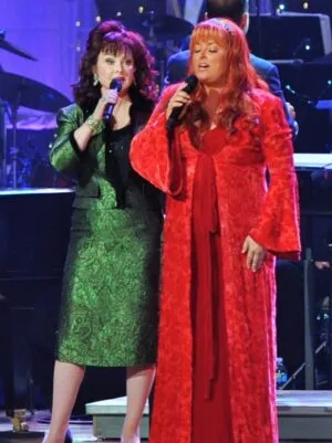 Wynonna and Naomi Judd sing onstage together in their story of faith