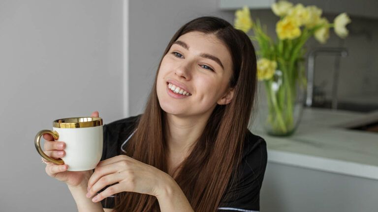 Woman smiling about gratitude vs thankfulness while she drinks coffee in the morning