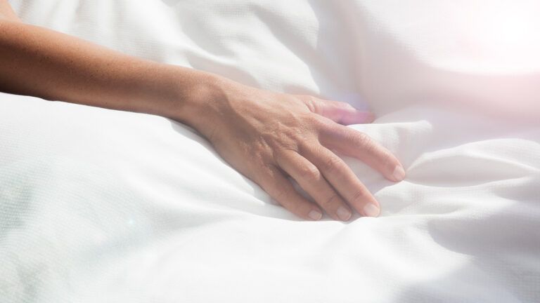 A woman's hand rests on a hospital blanket
