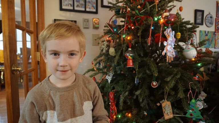 Kelly Gallagher’s son, Hudson, standing in front of a Christmas tree; Photo Courtesy Kelly Gallagher