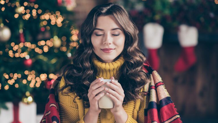 Woman closing her eyes, standing next to a Christmas tree; Getty Images
