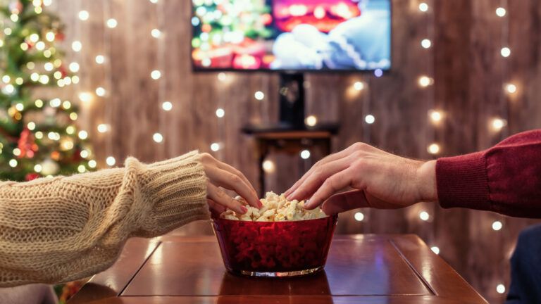 Two people's hands reach for popcorn while they watch advent movies