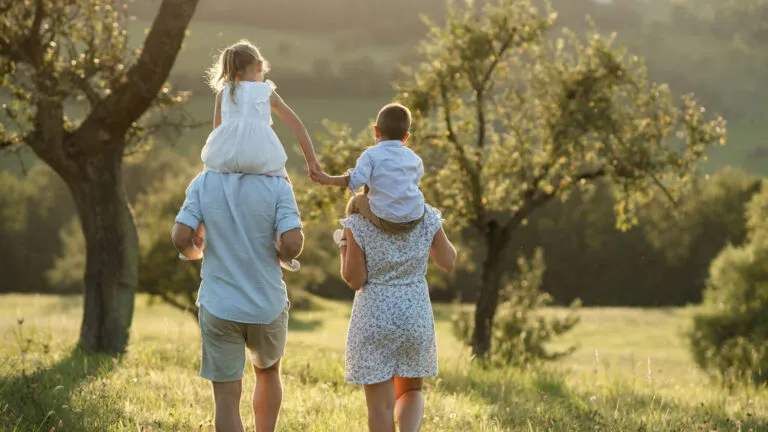 Family of four walking through a lush, green meadow.