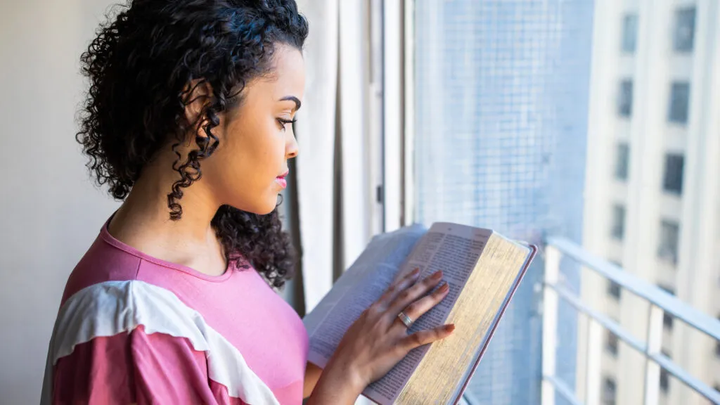 A woman reading by the window to develop her daily devotional habit