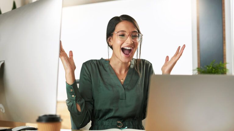 Businesswoman at her laptop looking excited after doing her micro habit for success