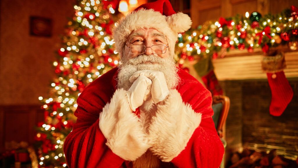 Portrait of Santa Claus in front of a Christmas tree wondering does Santa Claus belong in Christmas