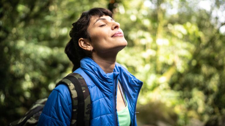Woman hiking out in nature with her eyes closed for her healthy bible habits