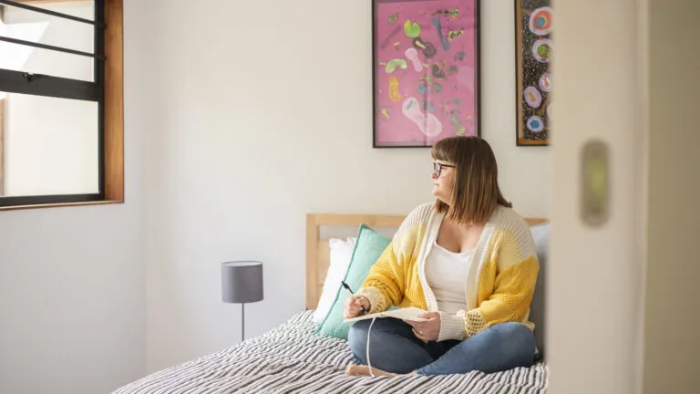 Woman sitting on her bed and writing in her journal about keeping her micro habits