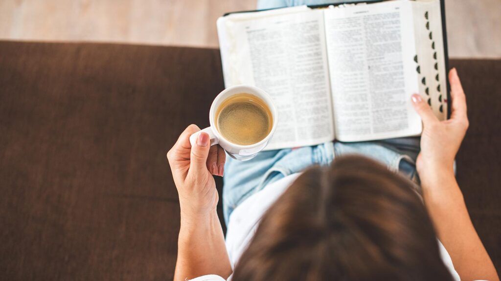 A woman reads her Bible with a cup of coffee in hand