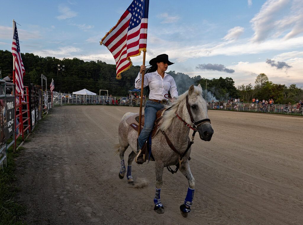 A cowgirl rides with an American flag; photo by Wade Payne