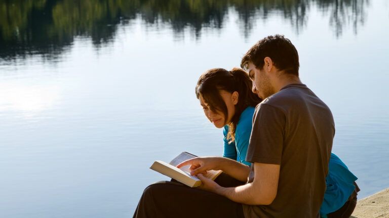 A couple reading the Bible by a lake to build the faith in their marriage