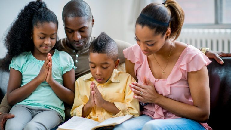 Family praying together on the couch with a bible opened to the lent story