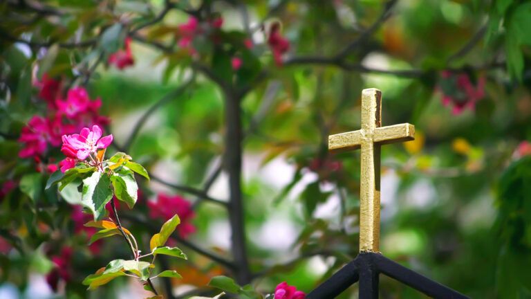 Golden cross on a fence surrounded by spring flowers to show lent in the bible