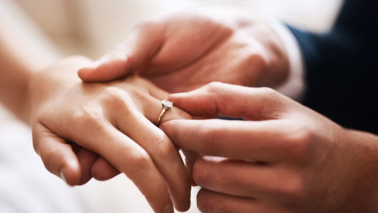 Groom putting a wedding ring on his bride's finger at their wedding with Bible verses about love