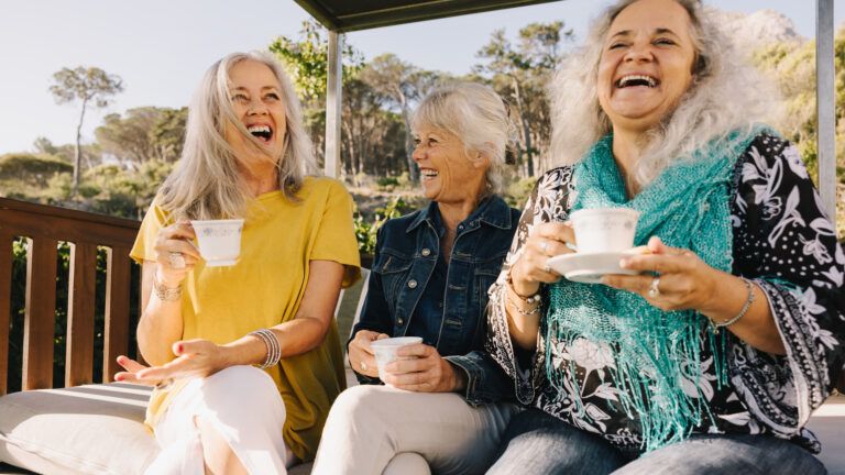 Group of women friends sitting together outside and laughing at happiness quotes for Friday