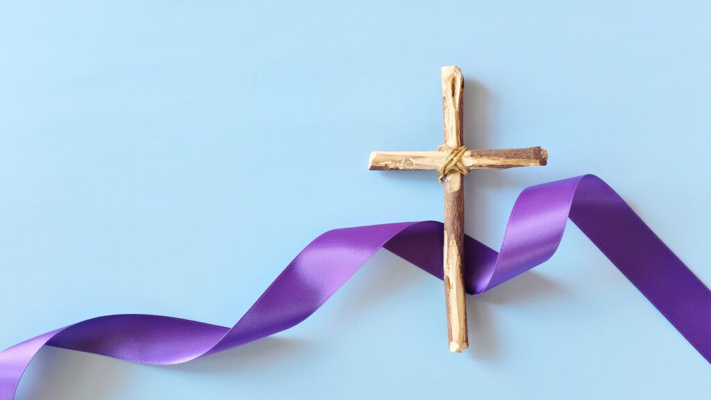 A wooden cross and purple ribbon signifying the meaning of lent