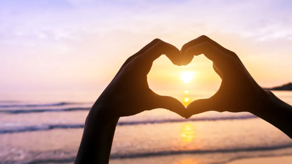 Two hands making a heart shape at sunset to show God's love for them