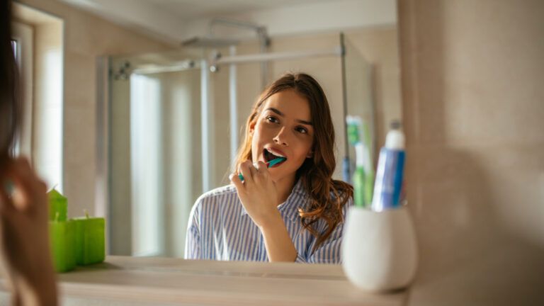 Woman brushing her teeth in the mirror for her new habit