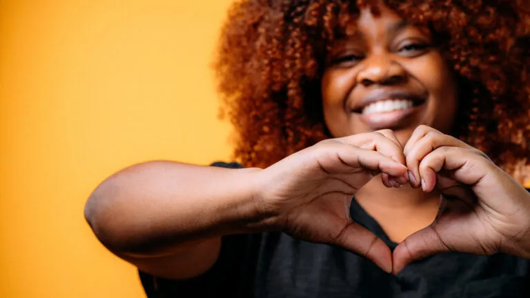 Woman holding up her hands in the shape of a heart to show Bible verses about love