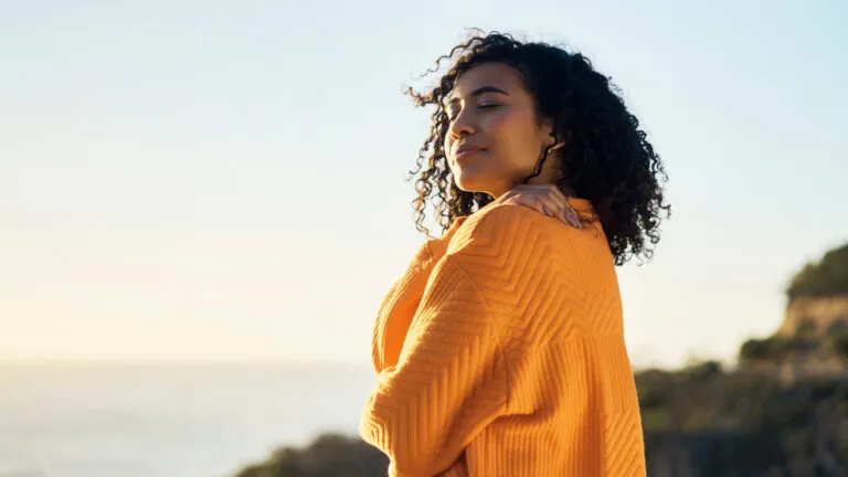 Woman hugging herself outside to show Bible verses about loving herself