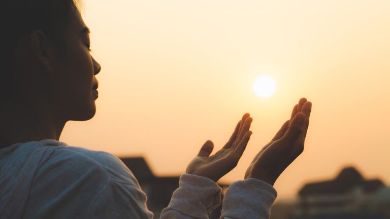 Woman with her arms up at sunset to pray for bible verses about love