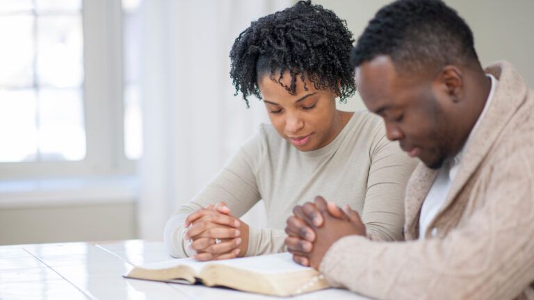 A couple praying together over a Bible for faith in marriage