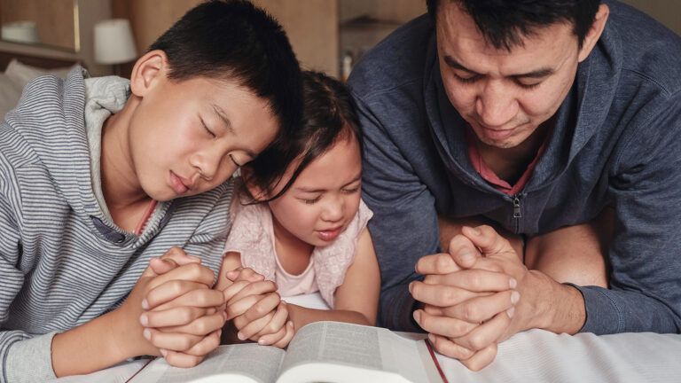 A family prays over an open Bible; Getty Images