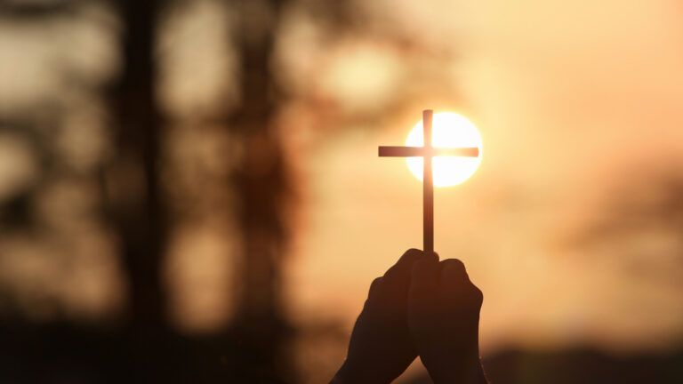 Hand holding up a cross to the sun