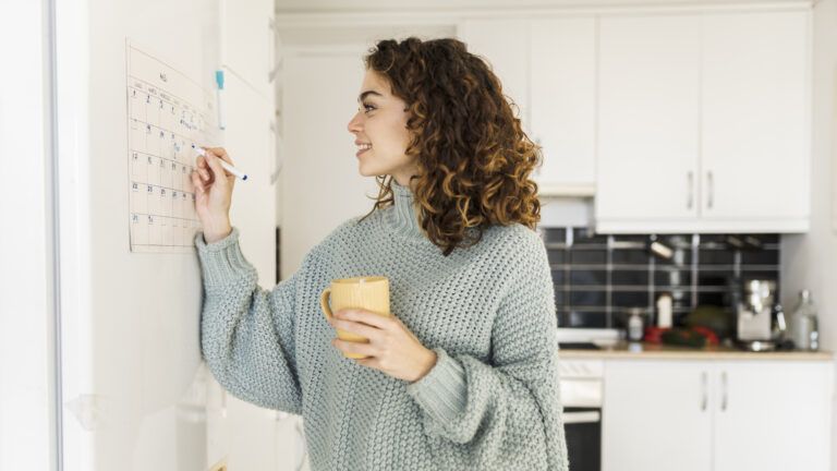 Woman in a light blue sweater marks her lent plan with goals on her kitchen calendar