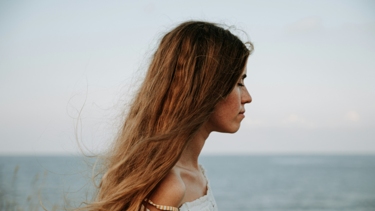 Woman by the ocean with eyes closed.