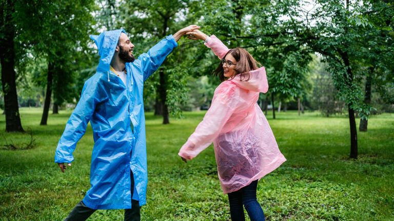 Smiling couple in raincoats dance in the rain for their spring activity