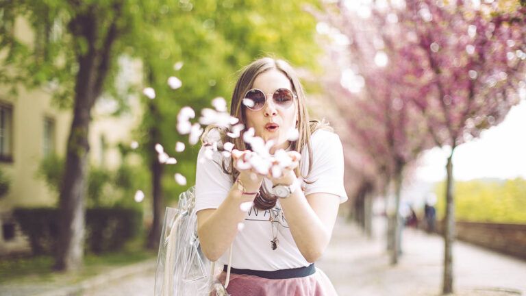 Woman in sunglasses blowing spring flower petals